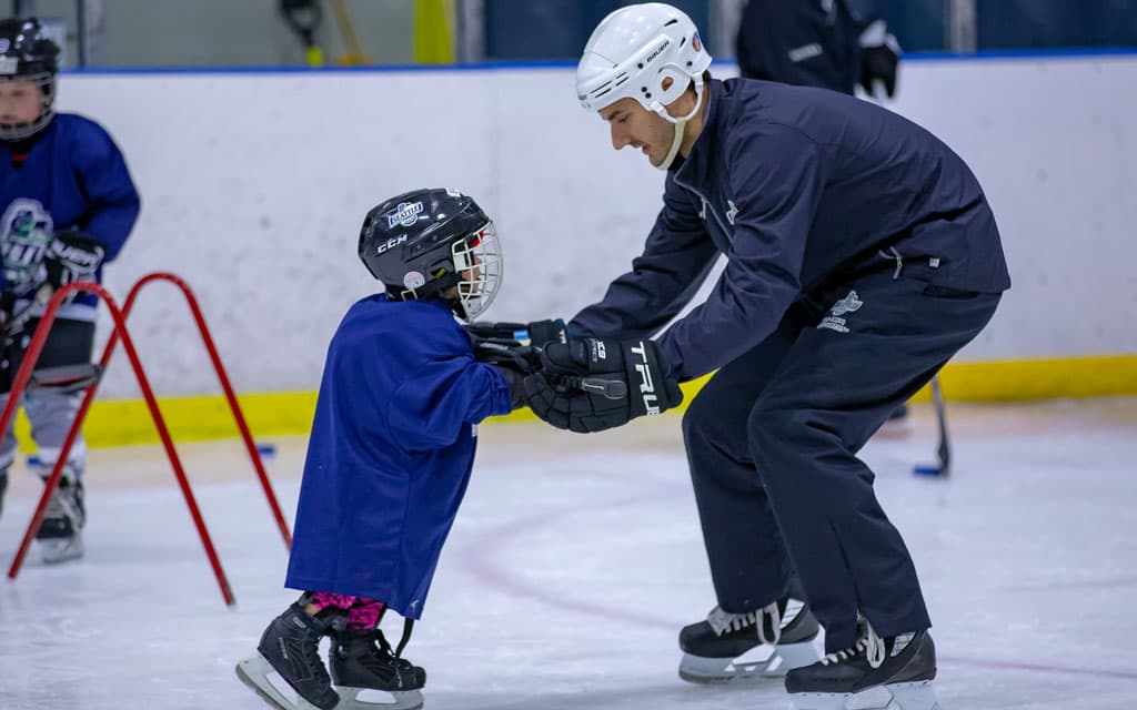 Coach helping tot learn to ice skate