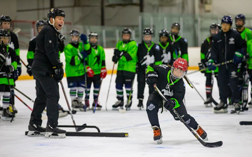Group of youth hockey players and coach watching a player shoot during a drill